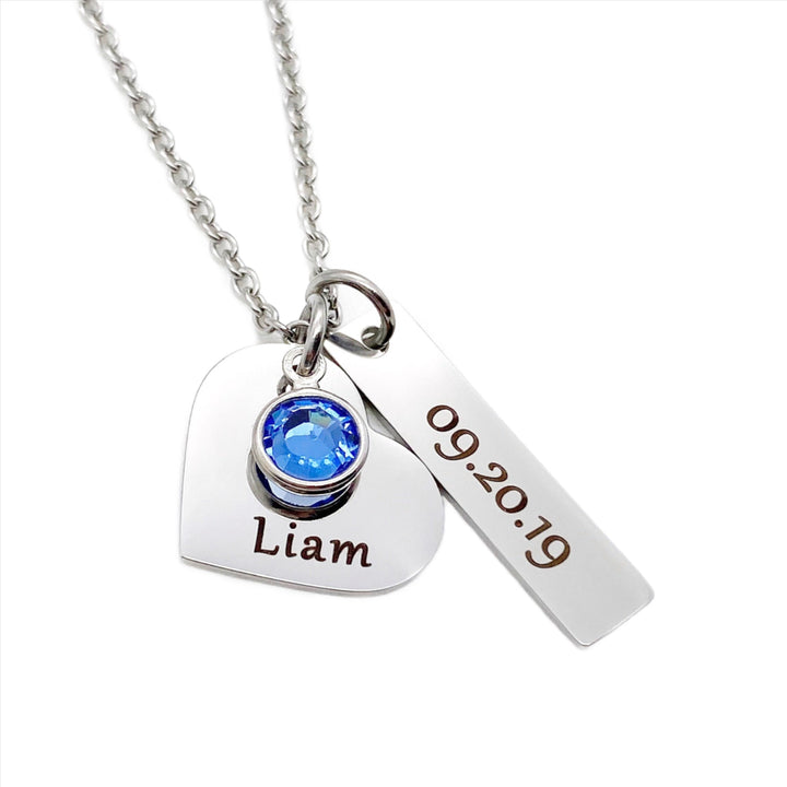 silver stainless steel necklace with a 3/4 inch engraved heart with the name Liam and a september blue birthstone. Next to the heart hangs a 1" rectangle charm with the date of birth 09.20.19