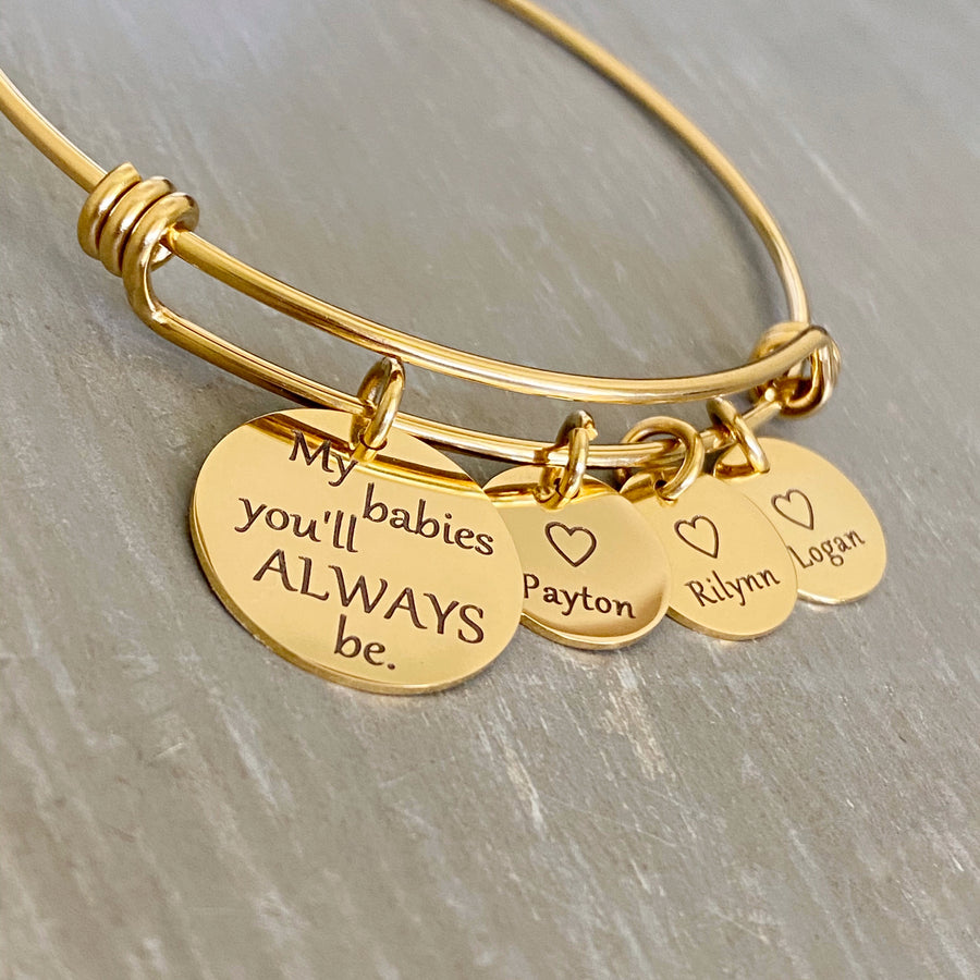 Yellow gold bangle charm bracelet with a 3/4" disc engraved with "my babies you'll always be." and a 1/2" engraved disc with an open heart and the name Payton, a second charm disc with the name Rilynn, and a third name disc with the name Logan.