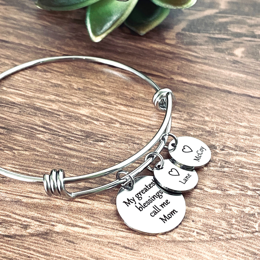 stainless steel silver bangle charm bracelet. first charm is engraved with the sayin g"my greatest blessings call me mom" next is a small 1/2" charm tag engraved with a heart and the name Lane. Next is a 1/2" charm engraved with a heart and the name McCoy