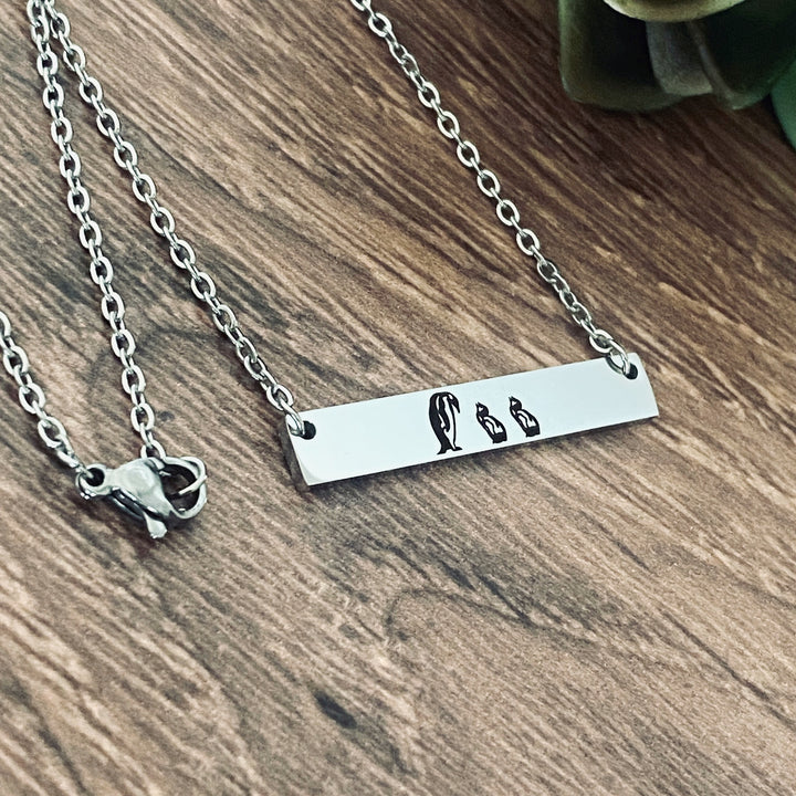Silver mother's penguin  horizontial bar necklace engraved with a mom penguin and 2 baby penguins attached to a silver cable chain with lobster clasp