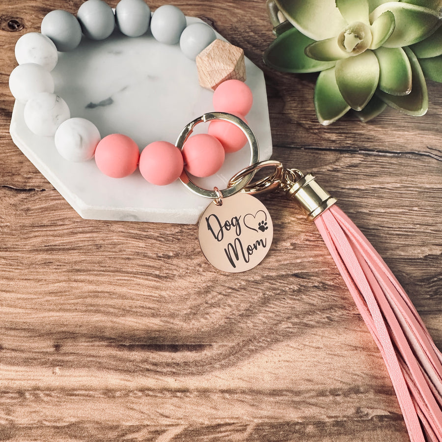 pink, marble, and grey round silicone beaded wristlet bracelet with a large lobster clasp keychain with matching leather tassel and charm tag engraved with Dog Mom and open heart dog paw print.