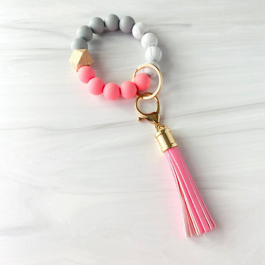 Pink, marble, grey silicone beaded bracelet. A rose gold lobster key hook with Pink tassel is attached to the wristlet