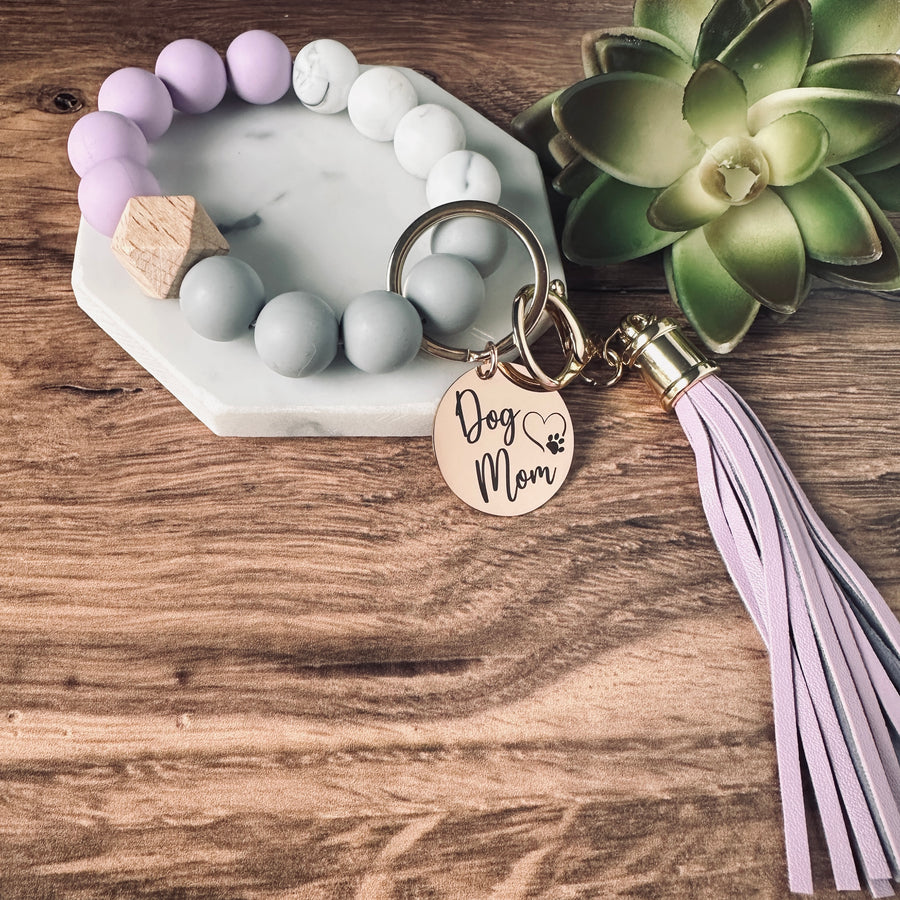 purple, marble, and grey round silicone beaded wristlet bracelet with a large lobster clasp keychain with matching leather tassel and charm tag engraved with Dog Mom and open heart dog paw print.