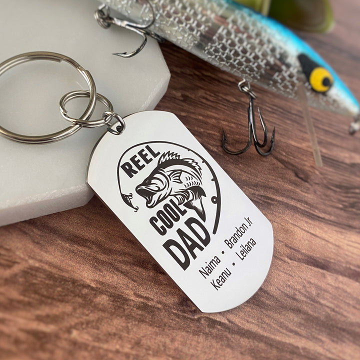 silver dog tag keychain engraved with a bass fish, fishing pole, and "Reel Cool Dad" along with children's names