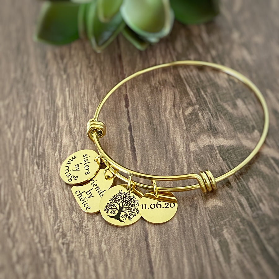 Yellow  gold Sister in Law  charm bracelet with 4 charms. First charm is engraved with "sister by marriage". next is a tree of life symbol char. next is a heart charm engraved with "friends by choice" last charm is a round charm engraved with date "11.6.20"