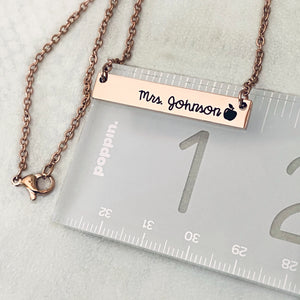 Rose Gold stainless steel horizontal  bar necklace engraved with "Mrs. Joshnson" and an apple charm. attached to a stainless steel cable chain on a ruler