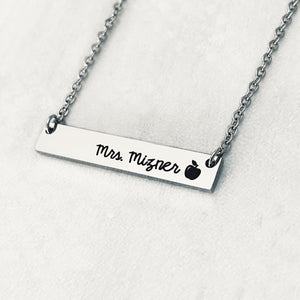 Silver stainless steel horizontal  bar necklace engraved with "mrs. Mizner" and an apple charm. attached to a stainless steel cable chain