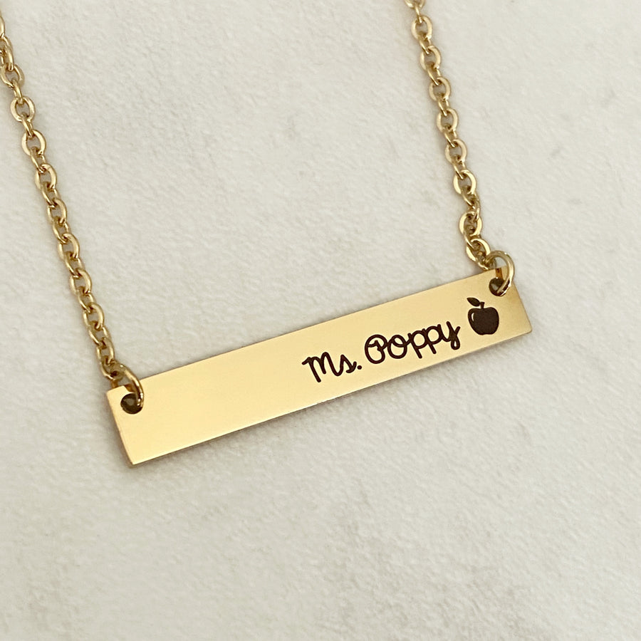 Yellow Gold stainless steel horizontal  bar necklace engraved with "Mrs. Poppy" and an apple charm. attached to a stainless steel cable chain