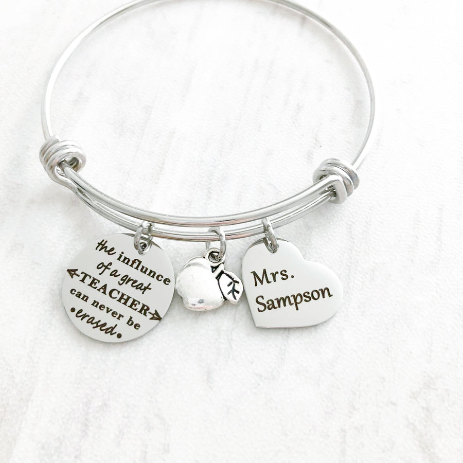 silver teacher bangle charm bracelet with engraved "the influence of a great teacher can never be erased" an apple charm and a 3/4" heart engraved with teachers name "mrs sampson""