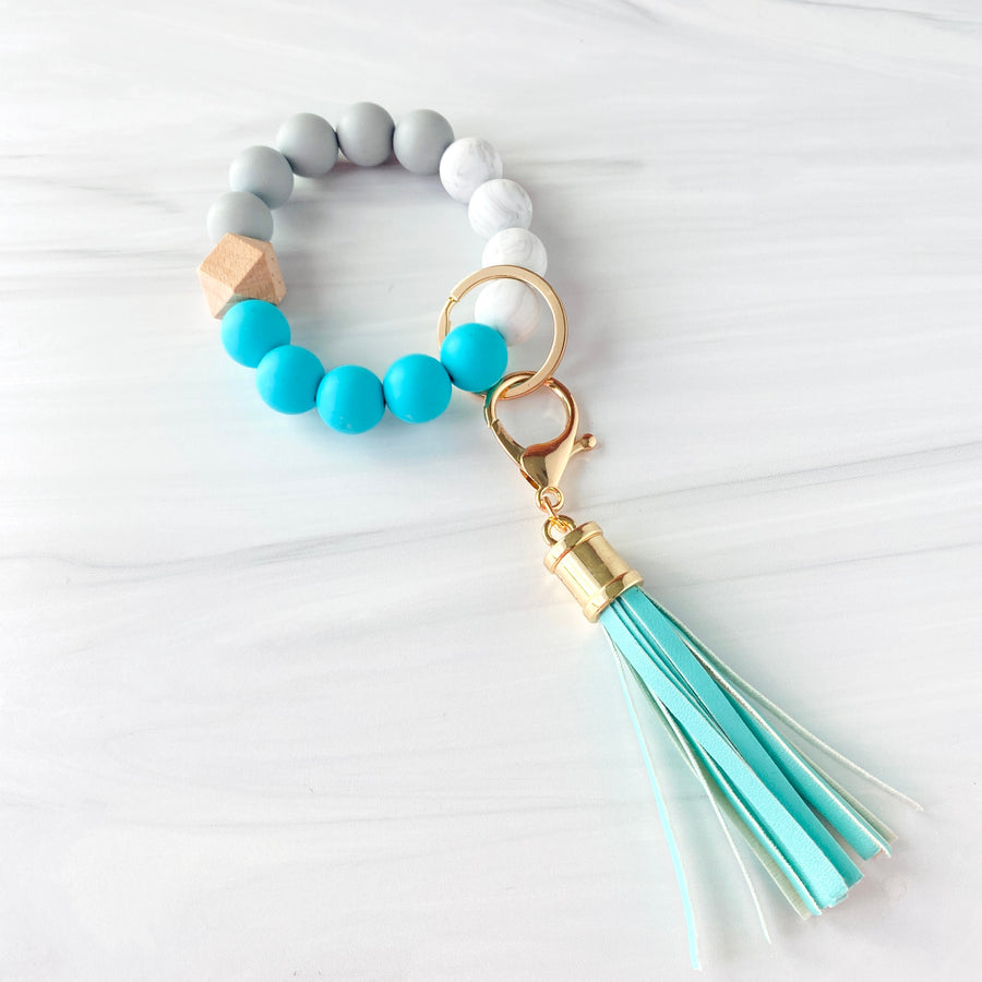 Turquoise, marble, grey silicone beaded bracelet. A rose gold lobster key hook with turquoise tassel is attached to the wristlet