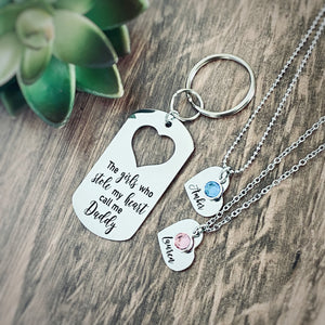 Silver Stainless Steel dog tag keychain engraved with "The girls who stole my heart call me Daddy". Next to the keychain are small heart necklaces. one with the name Lauren and a pink october stone and the second necklace with the name amber and a blue december stone
