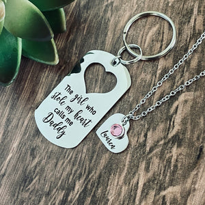 Silver Stainless Steel dog tag keychain engraved with "The girl who stole my heart calls me Daddy". Next is a 3/4" heart charm engraved with the name "Lauren" and a pink october stone. the charm is attached to a silver cable chain necklace