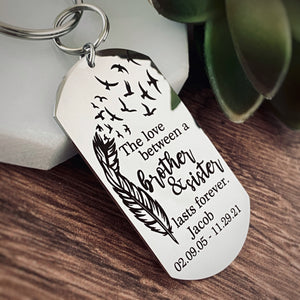 silver dog tag keychain attached to a split ring and then a 1" stainless steel keyring. Dog tag measures 1 inch by 2.25" and has black engraving with a feather that fades into birds flying into the air. The phrase "The love between a brother & Sister lasts forever." Personalized on the bottom of the dog tag is engraved with the name Jacob and the date of birth 02.09.05 and the death 11.29.21
