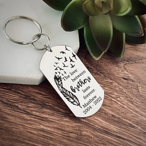 silver dog tag keychain attached to a split ring and then a 1" stainless steel keyring. Dog tag measures 1 inch by 2.25" and has black engraving with a feather that fades into birds flying into the air. The phrase "The love between brothers lasts forever." Personalized on the bottom of the dog tag is engraved with the name Matthew and the year of birth 2004 and the death year 2022
