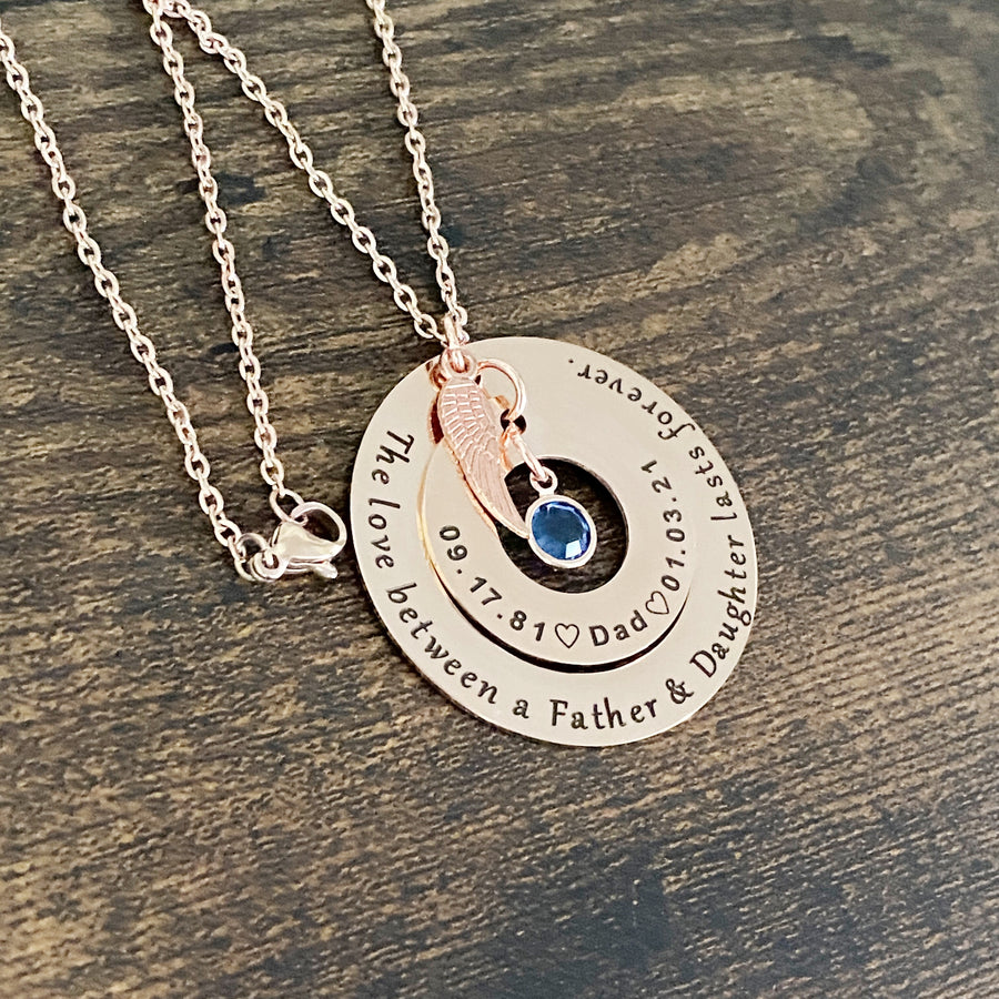 engraved rose gold memorial necklace engraved with "The love between a father and daughter lasts forever" and personalized with date of birth 9.17.81, Dad, and heaven date 1.3.21" and a blue september birthstone and angel wing charm. pendant attached to a cable chain