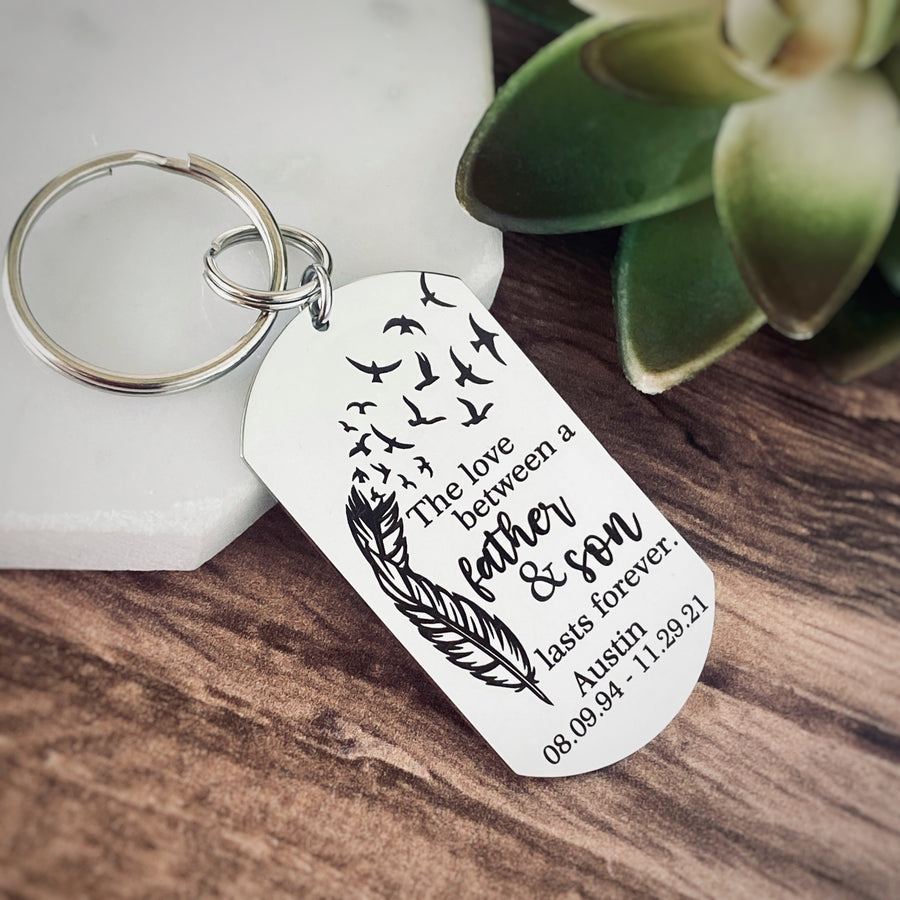 silver dog tag keychain attached to a split ring and then a 1" stainless steel keyring. Dog tag measures 1 inch by 2.25" and has black engraving with a feather that fades into birds flying into the air. The phrase "The love between a Father & Son lasts forever." Personalized on the bottom of the dog tag is engraved with the name Austin and the date of birth 08.09.94 and the death date 11.29.21