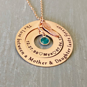 Rose Gold Round 2 disc necklace. outside washer is engraved with "the love between a mother and daughter lasts forever." The inner washer is engraved with the birthdate 12.27.90 a heart image the name Mya, heart image, and death date 7..04.17. May birthstone dangles inside the washer and angel wing charm on top. All charms and pendants hang from a stainless steel cable chain
