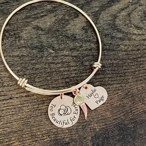 Rose Gold stainless steel trip loop expandable bangle charm bracelet. first charm is engraved with twin babies under angel wings along with the saying "Too beautiful for earth". next is a heart charm engraved with the names haylee and paige next is the twins august birthstone and an angel wing charm.