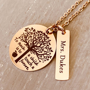 A 1 inch round stainless steel plated rose gold disc engraved with a tree of life symbol and the verbiage "To teach a child is to touch a future." Next to the disc is a 1.2" rectangle engraved with "Mrs. Dukes". The charms are attached to a rose gold cable chain.