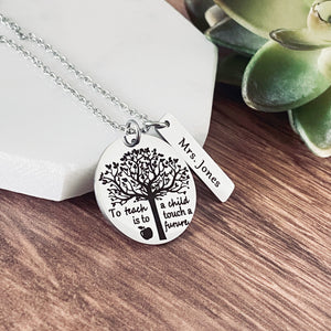 A 1 inch round stainless steel silver round pendant engraved with a tree of life symbol and the verbiage "To teach a child is to touch a future." Next to the disc is a 1.2" rectangle engraved with "Mrs. jones". The charms are attached to a silver cable chain.