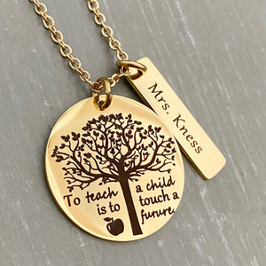A 1 inch round stainless steel plated yellow gold disc engraved with a tree of life symbol and the verbiage "To teach a child is to touch a future." Next to the disc is a 1.2" rectangle engraved with "Mrs. Kness". The charms are attached to a yellow gold cable chain.