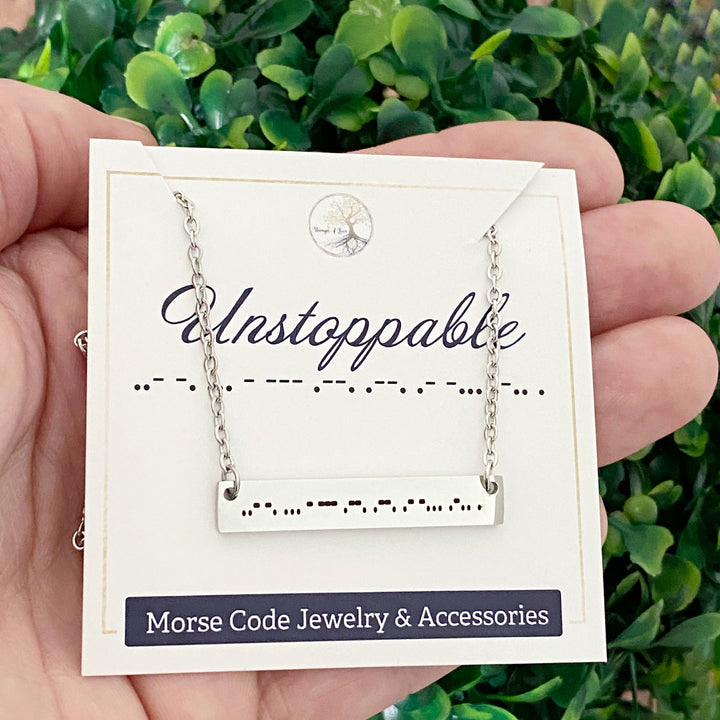 Silver Stainless steel laser bar necklace engraved with "Unstoppable" in Morse Code. Necklace is on a placement card telling what. the morse code stands for 