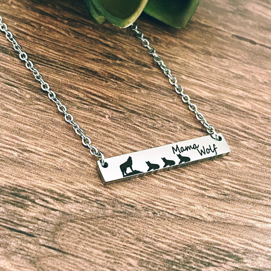 silver stainless steel bar necklace engraved with "mama wolf" a mom wolf image and 3 wolf cubs. attached to a silver stainless steel cable chain with lobster clasp