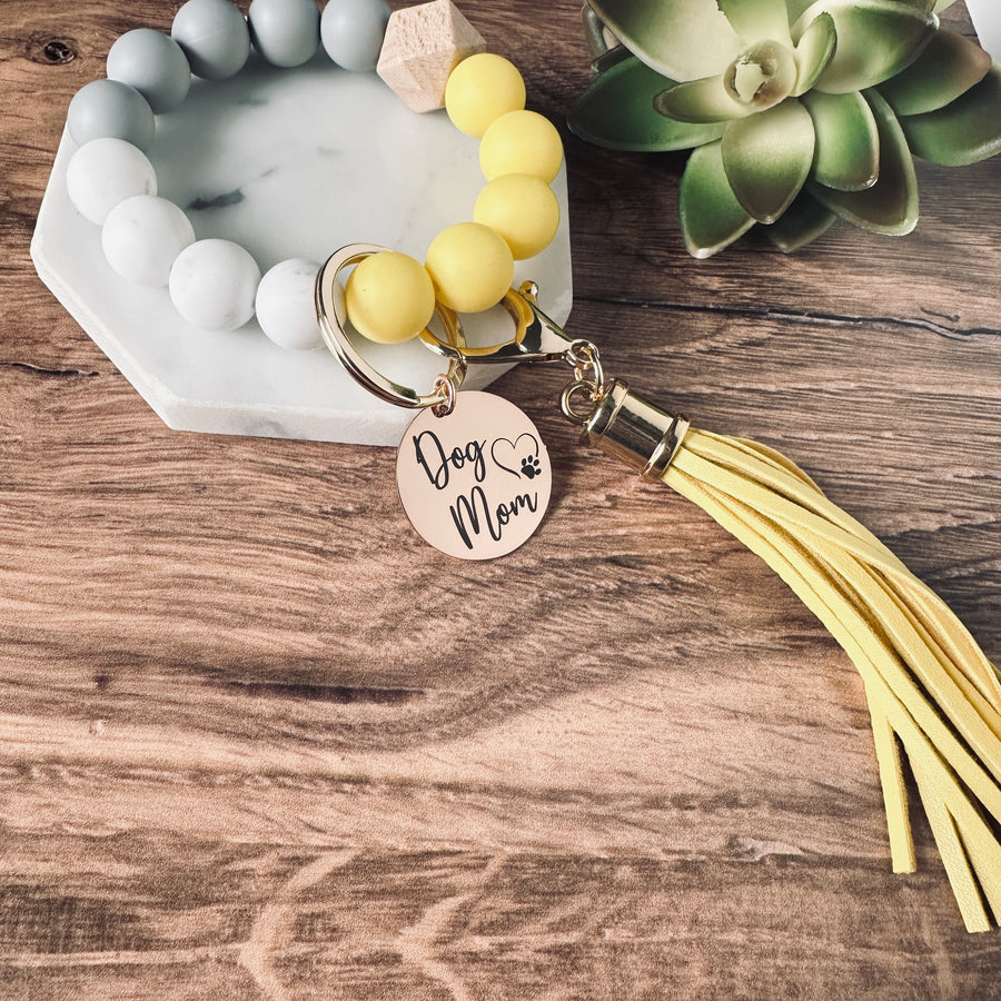 Yellow, marble, and grey round silicone beaded wristlet bracelet with a large lobster clasp keychain with matching leather tassel and charm tag engraved with Dog Mom and open heart dog paw print.