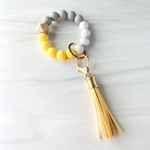 Yellow, marble, grey silicone beaded bracelet. A rose gold lobster key hook with yellow tassel is attached to the wristlet