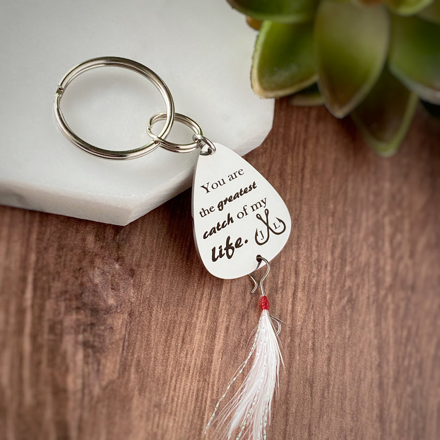 Silver Stainless steel fishing lure keychain engraved with the phrase, "You are the greatest catch of my life." and a double fishing hooks with the initials J and L. attached to the lure is a fishing feather
