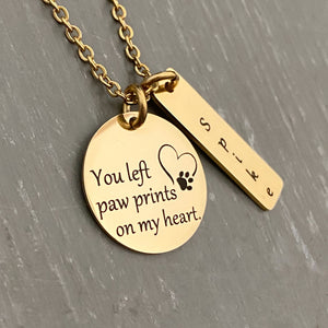 yellow gold 3/4 inch pendant engraved with "you left paw prints on my heart" with an image of a heart and paw print. Next to it is a rectangle tag personalized with the name spike. Pendants are attached to a cable chain.