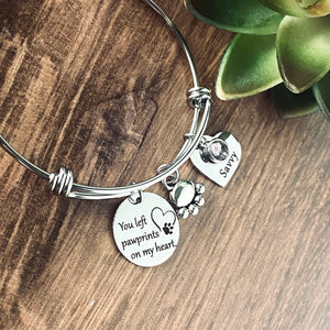 silver stainless steel triple loop bangle charm bracelet. Big disc is 3/4" engraved with the phrase, " You left pawprints on my heart". next is a pawprint charm, lastly is a 3/4" heart charm engraved with dog's name "savvy" and a june birthstone.