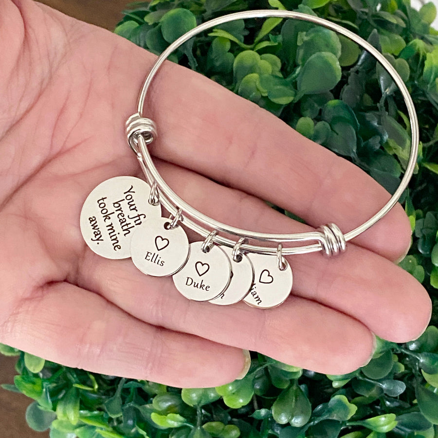 stainless steel silver bangle charm bracelet with a 3/4 inch disc engraved with "your first breath took mine away". 1/2 inch name discs with open heart image above the engraved name on a womens hand to show size