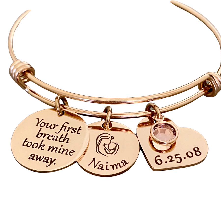 rose gold triple loop wire bracelet with a round 3/4 inch engraved with "your first breath took mine away", a 5/8 inch round disc with engraved name "Naima" with an image of a mom holding a baby, and a 3/4 inch heart engraved with the birthday date "6.25.08", and a june birthstone.