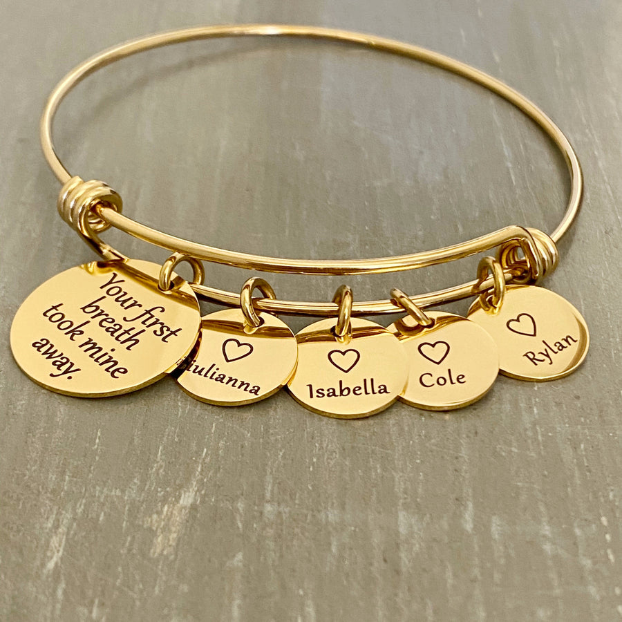 stainless steel yellow gold bangle charm bracelet with a 3/4 inch disc engraved with "your first breath took mine away". 1/2 inch name discs with open heart image above the engraved name. 