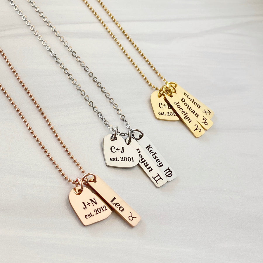 rose necklace with heart engraved "J + N est 2012" and 1 rectangle name tag with the taurus zodiac sign and name Leo. Silver necklace with "C + J ext 2001" and 2 name tags "Regan and gemini sign, Kelsey and a virgo sign. Gold necklace "C +. B est 2012" Jocelyn Aries symbol, Rowan Capricorn, Finley Sagittarius zodiac symbol 
