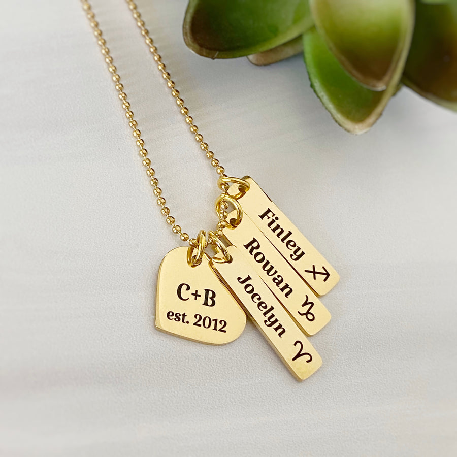 Gold mother's necklace with heart charm engraved "C+B est 2012". 3 name tags. jocelyn with aries symbol. Rowan with capricorn zodiac sign. Finley with Sagittarius zodiac symbol