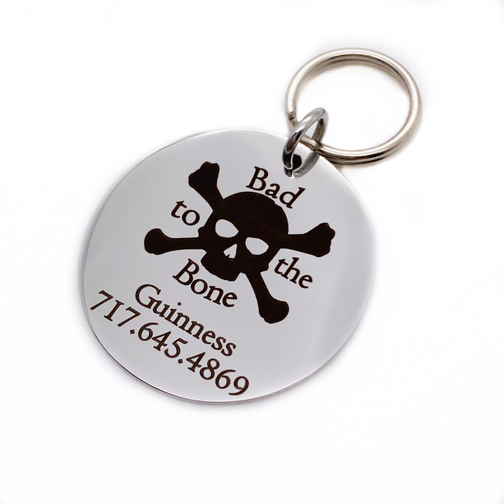 Silver stainless steel dog collar id tag with black engraving "Bad to the Bone" with a picture of cross bones, pets name and telephone number