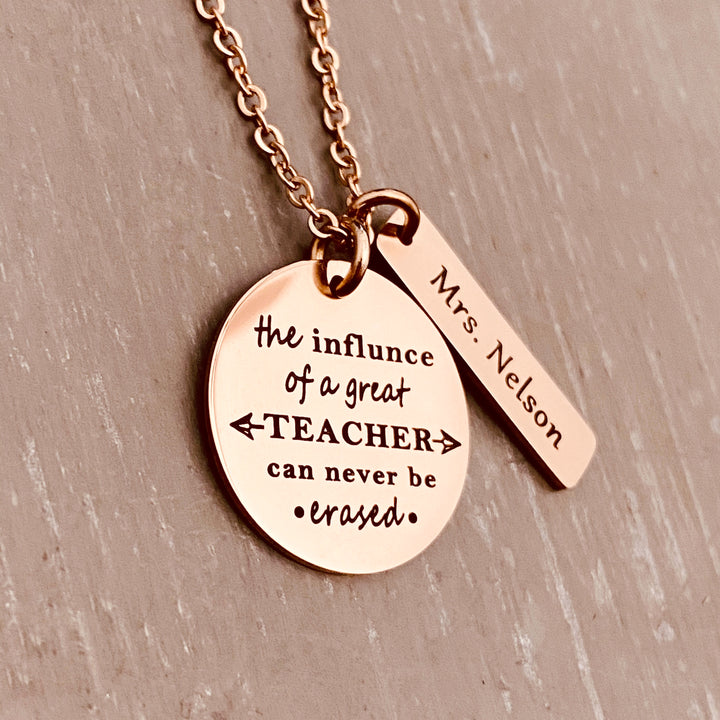 A 1 inch round stainless steel plated rose gold disc engraved with the verbiage "The influence of a great teacher can never be erased." Next to the disc is a 1.2" rectangle engraved with "Mrs. Nelson". The charms are attached to a rose gold cable chain.